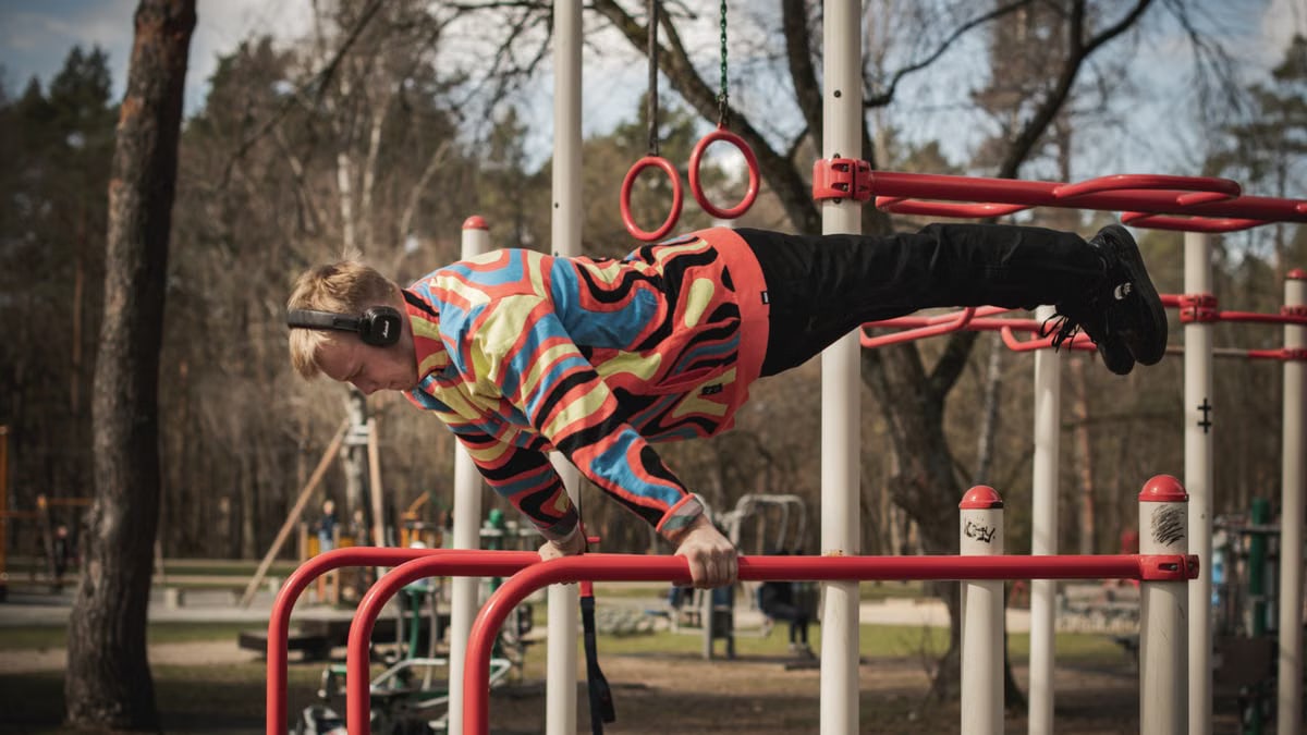 Young adult man exercises on outdoor gym bars in a colorful outfit in Vilnius, Lithuania.